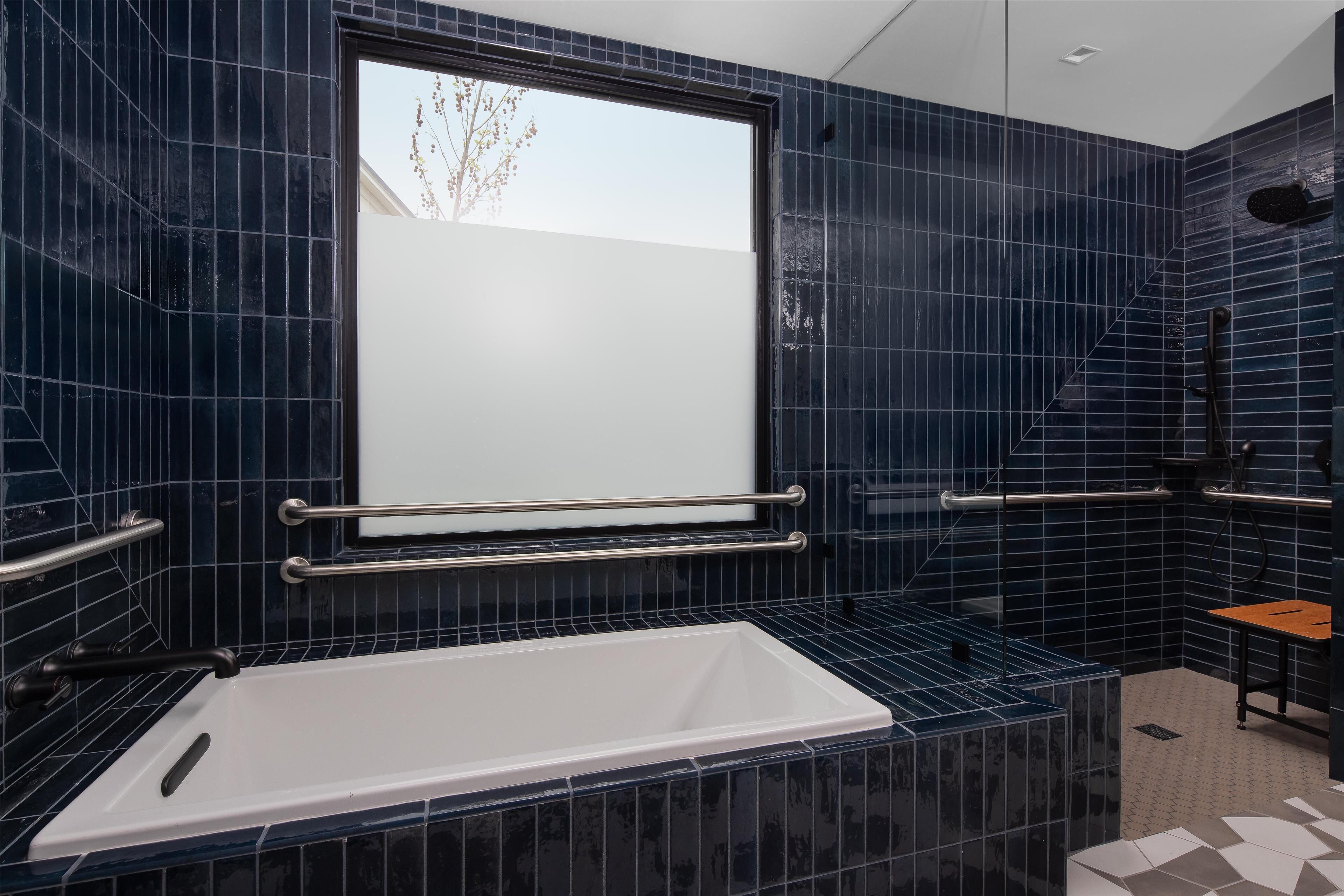 A modern bathroom with a bathtub, handrails, and a window.