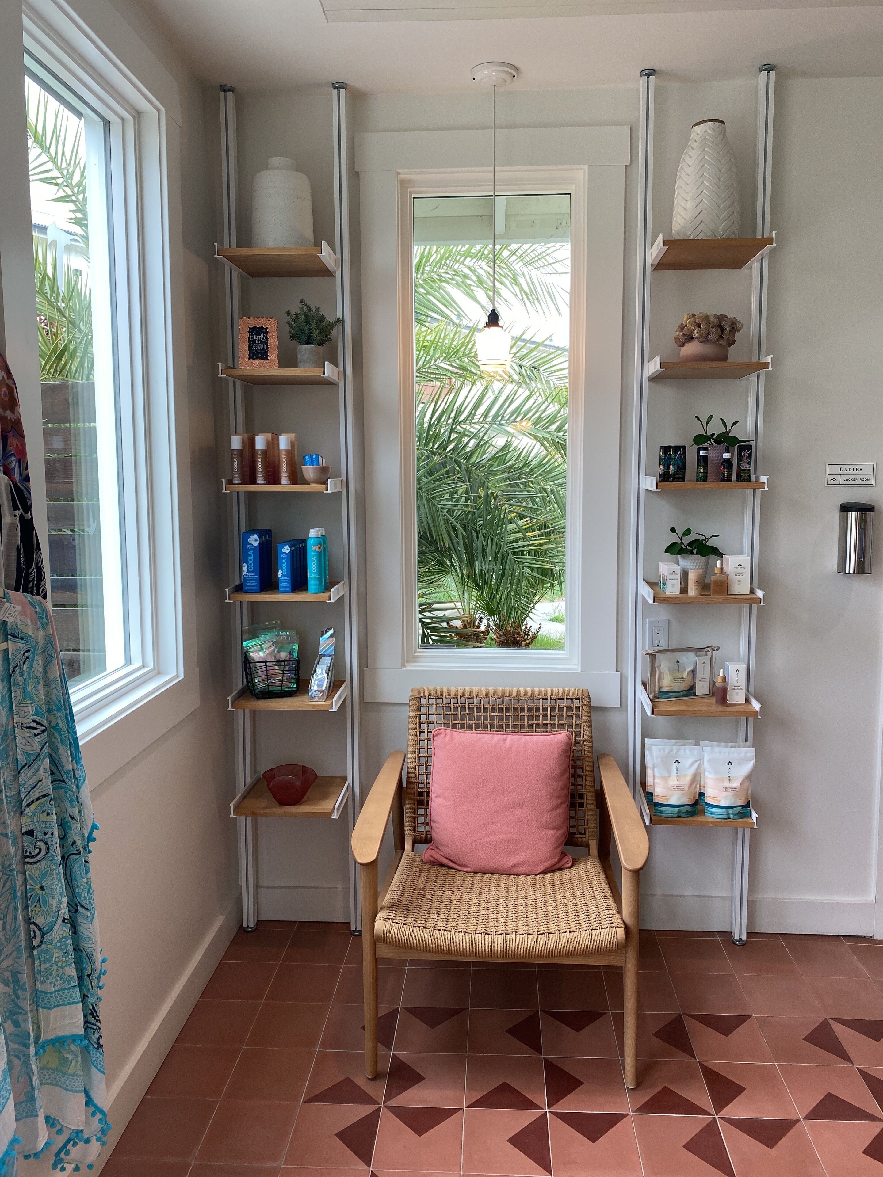 A room with a wicker chair, a window with a view of greenery, and shelves with various items.