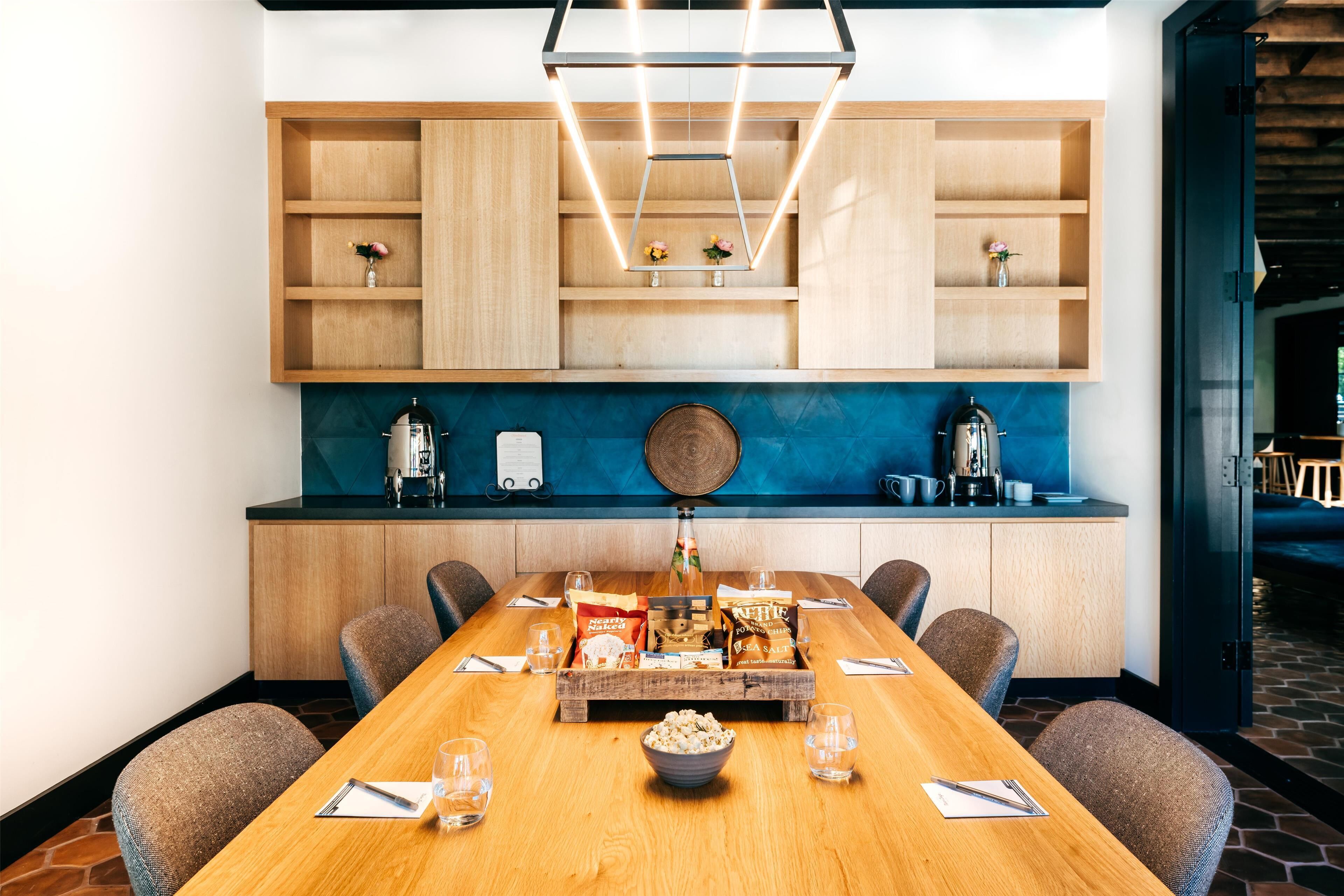 A conference room with a long wooden table, six chairs, a coffee machine, and a decorative bowl of snacks.
