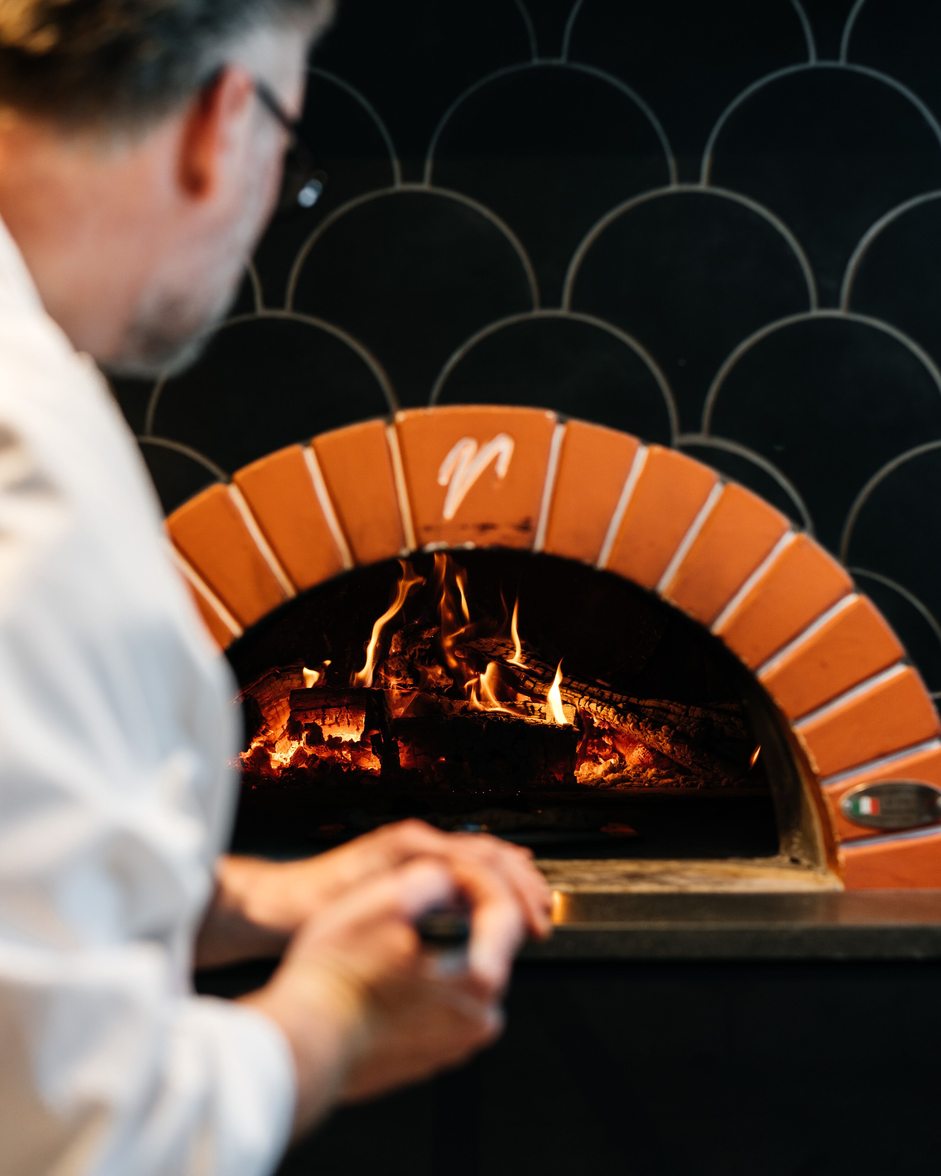 A person operating a brick oven pizza oven with a logo on the front.