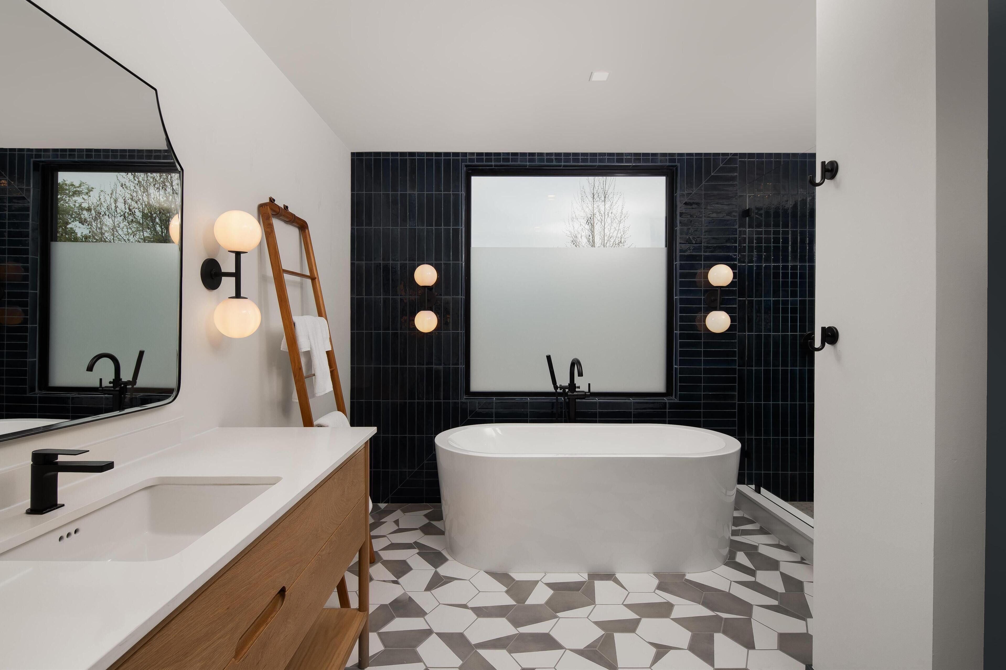 A modern bathroom with a freestanding bathtub, a large mirror, and a vanity with a wooden cabinet.
