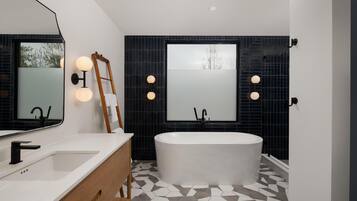 A modern bathroom with a freestanding bathtub, a large mirror, and a vanity with a wooden cabinet.