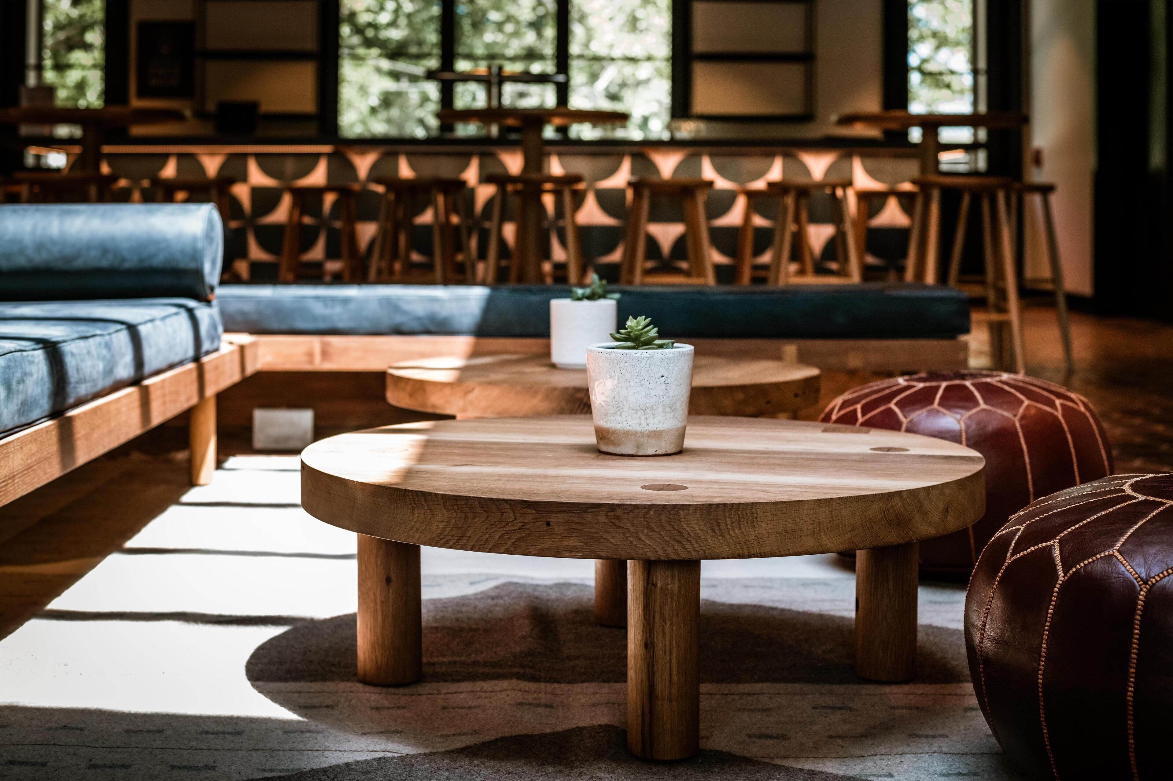 Un coin salon accueillant avec une table ronde en bois, un canapé bleu et un pouf à motifs.