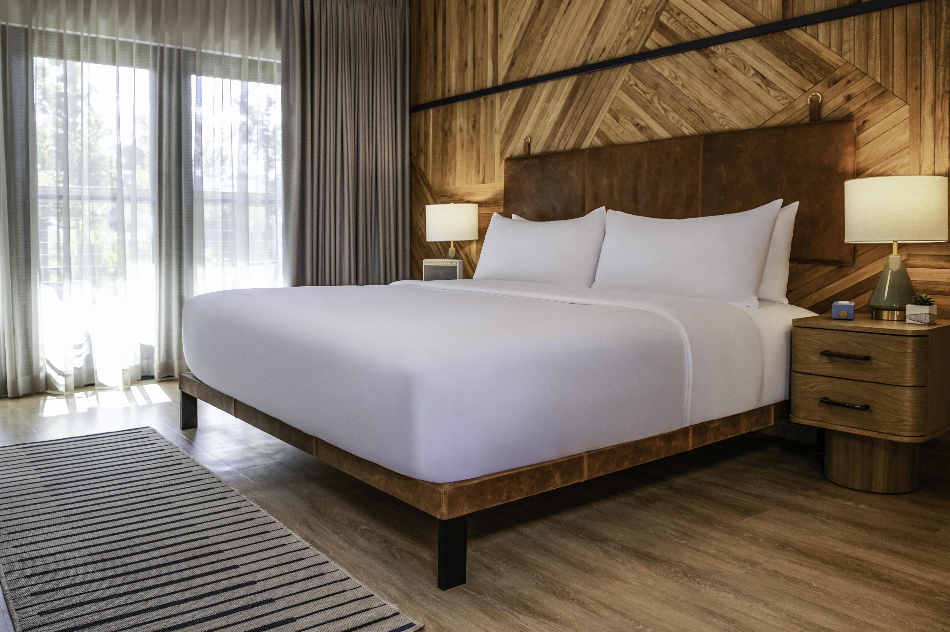 A large bed with white linens, two bedside tables with lamps, and a wooden headboard.