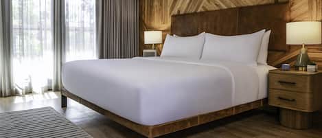 A large bed with white linens, two bedside tables with lamps, and a wooden headboard.