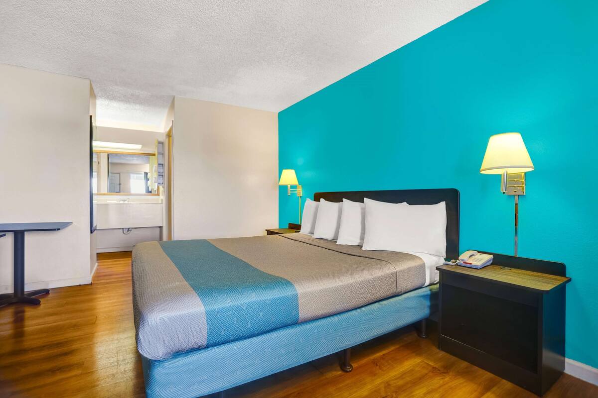 A hotel room with a bed, bedside tables, a desk, and a mirror.