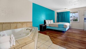 A modern hotel room with a large bathtub, a bed with blue bedding, and a view of the city through a window. - Motel 6 Fort Bragg, CA (Fort Bragg)