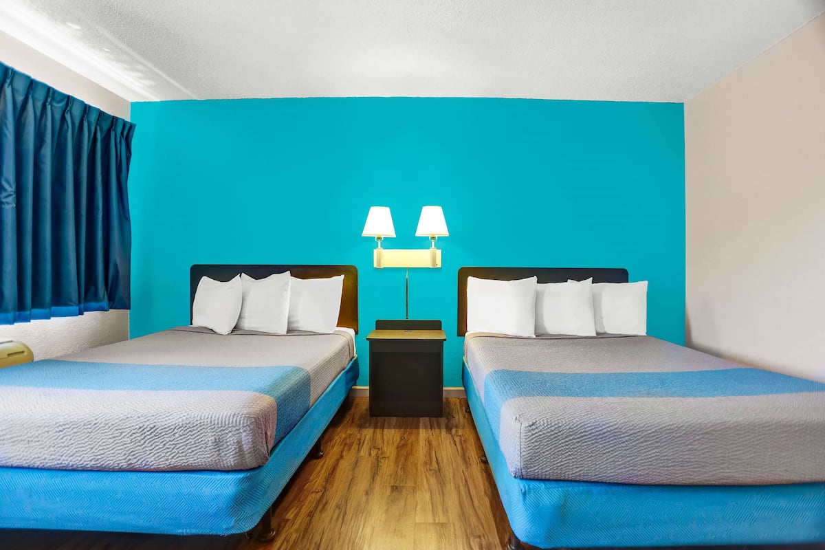 A hotel room with two beds, a nightstand, and a wall-mounted lamp.