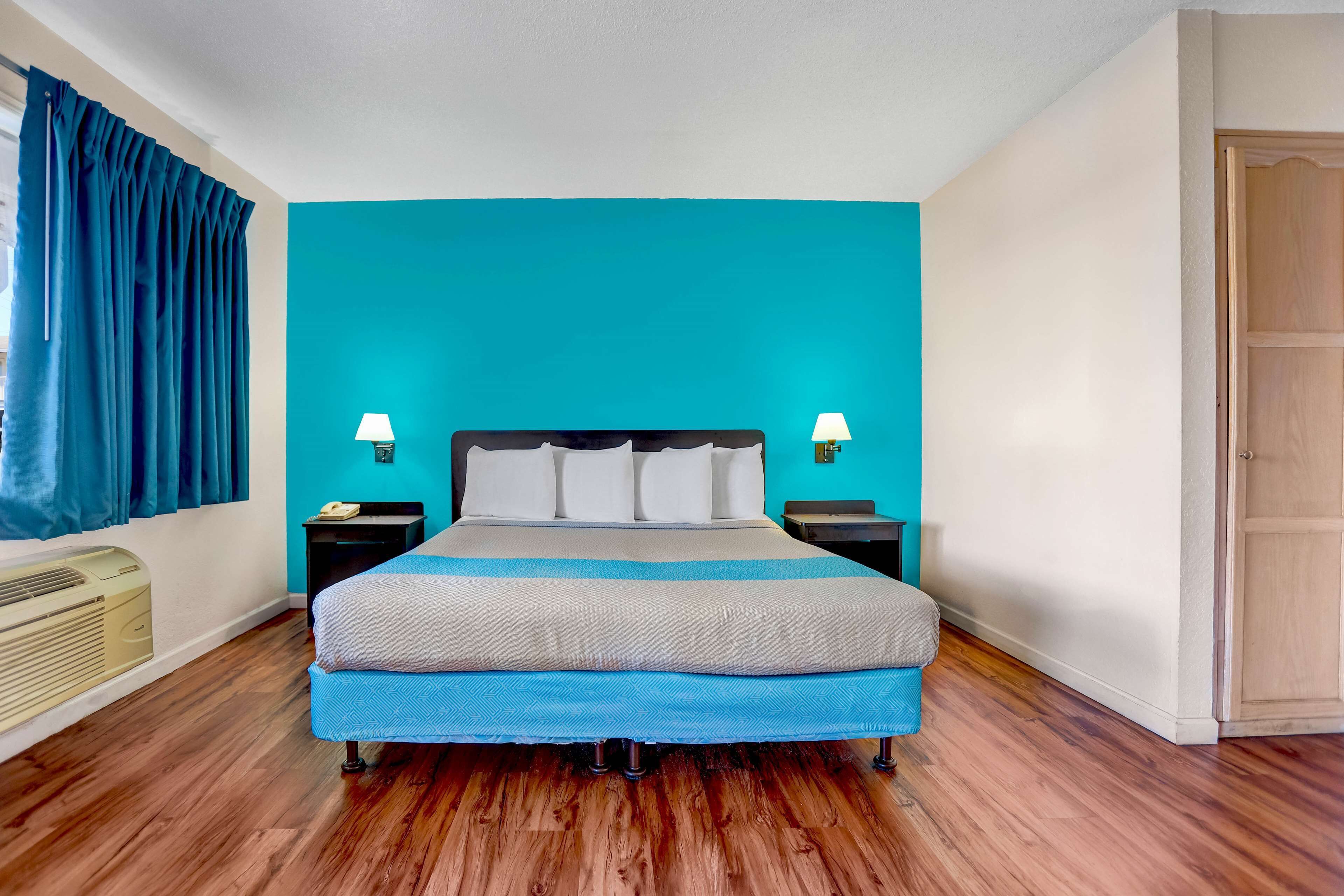 A hotel room with a large bed, two bedside tables with lamps, a blue wall, and a wooden floor.