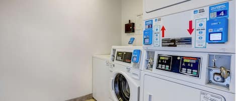 A laundry facility with multiple washing machines and dryers, a control panel, and instructional signage.