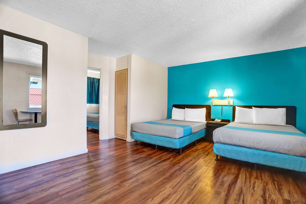 A hotel room with two single beds, a large mirror, wooden flooring, and a teal accent wall.