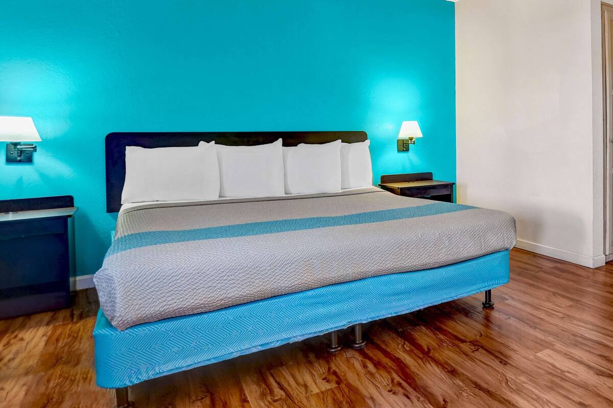 A bed with a blue and white patterned bedspread, two white pillows, and a headboard. There are two bedside tables with lamps, and the room has wooden flooring.