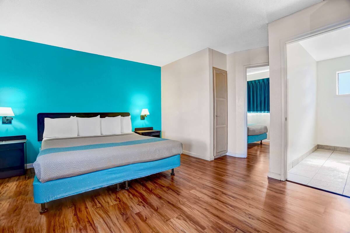 A modern hotel room with a large bed, wooden flooring, and a bright blue accent wall.