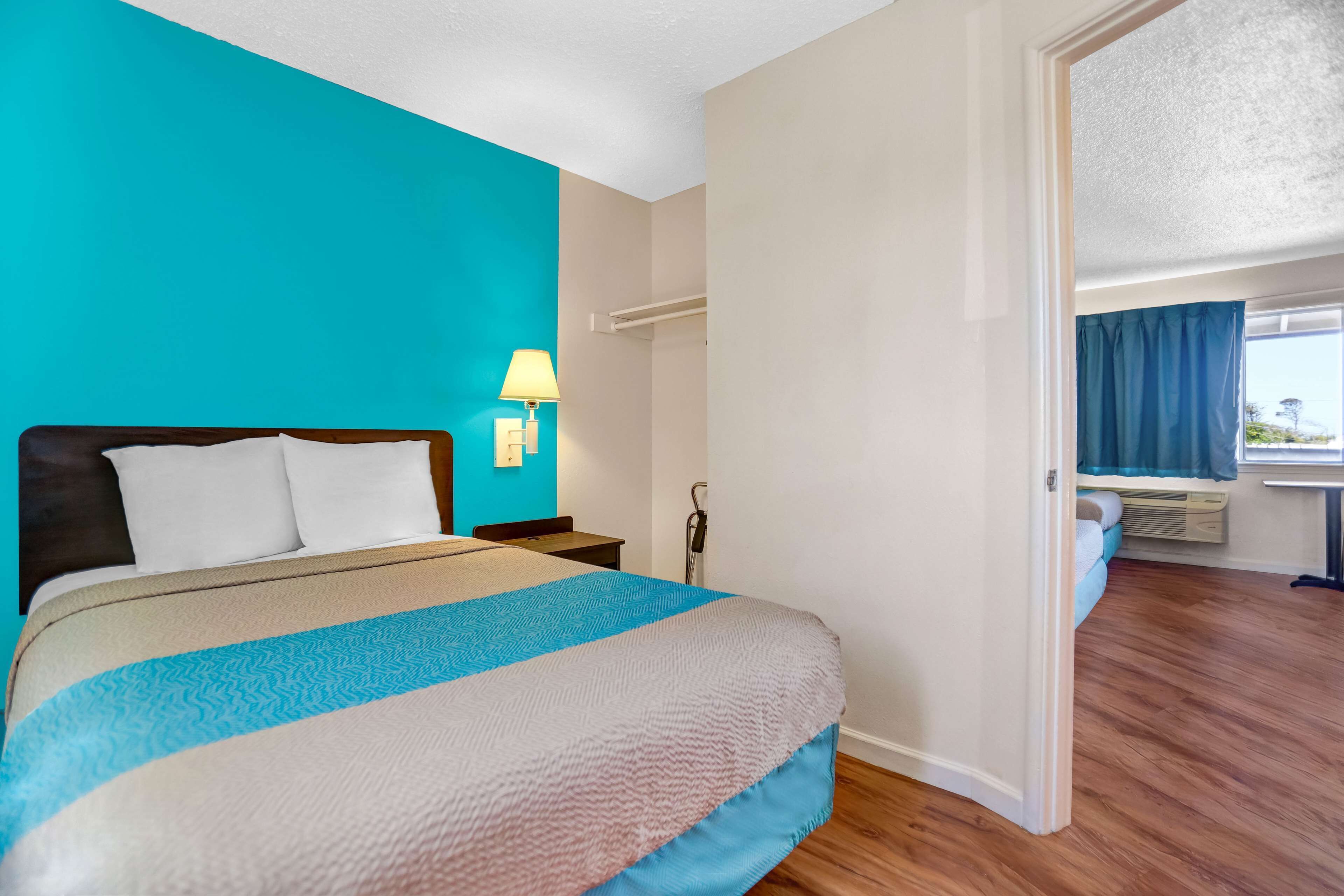 A hotel room with a bed, a nightstand, a lamp, and a window with curtains.