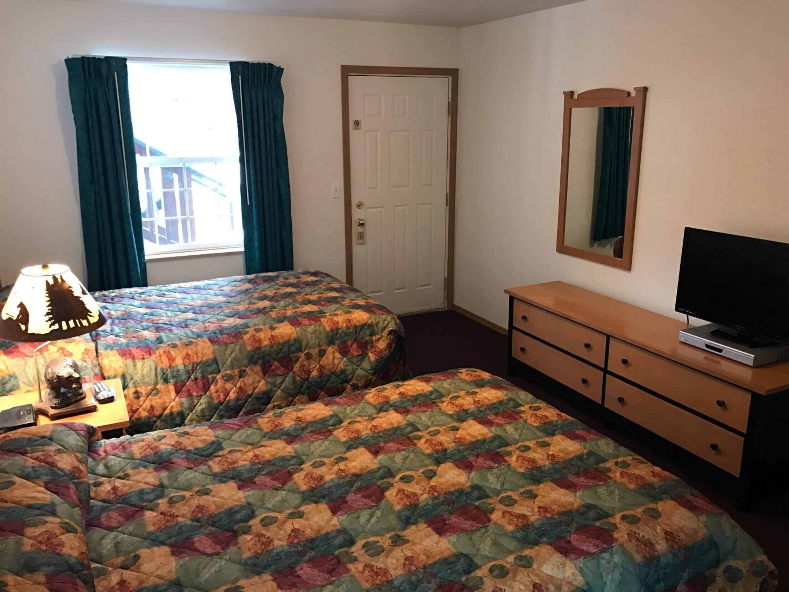 A room with two beds, a dresser, a television, and a window with curtains.