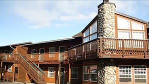 A two-story wooden building with a stone chimney, wooden balconies, and a staircase leading to the upper level. - Harborview Inn (Seward)