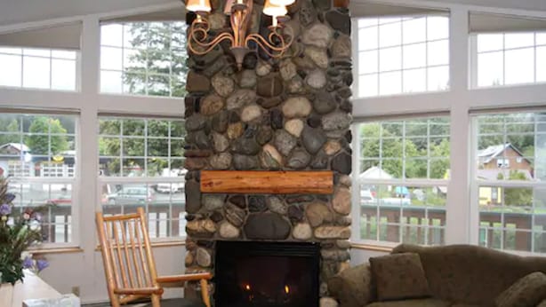 A cozy living room with a stone fireplace, a wooden rocking chair, and a sofa. - Harborview Inn (Seward)