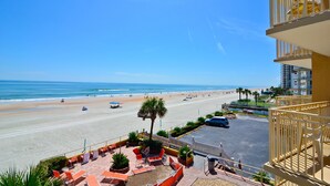 A beach view from a balcony with outdoor seating and a parking area.