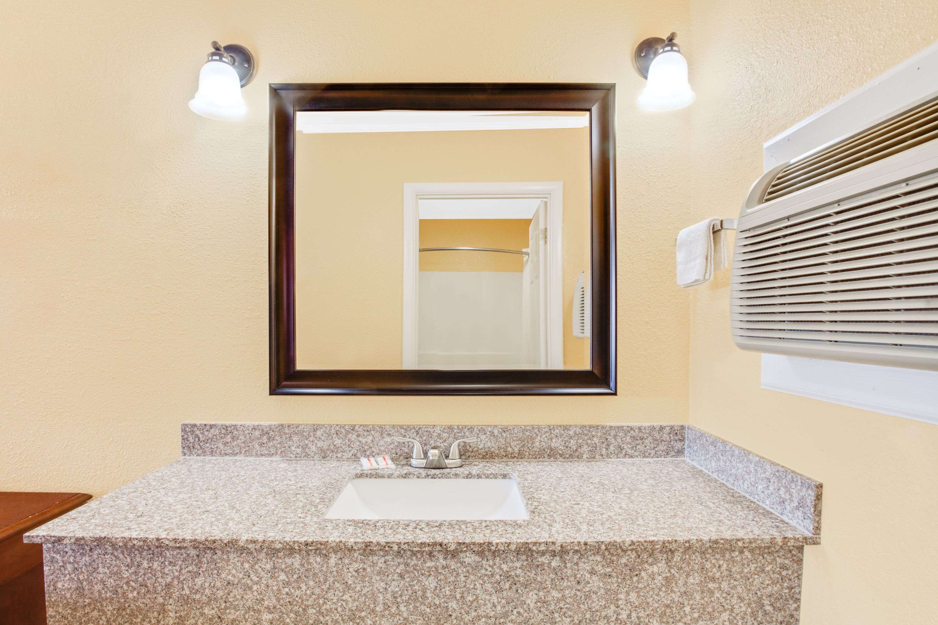 Un baño con lavamanos de encimera de granito, un espejo grande y un perchero para toallas.