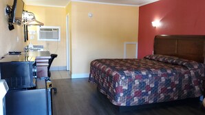 Une chambre d’hôtel de taille réduite, comprenant un lit, un bureau avec un ordinateur, une chaise et une petite table.