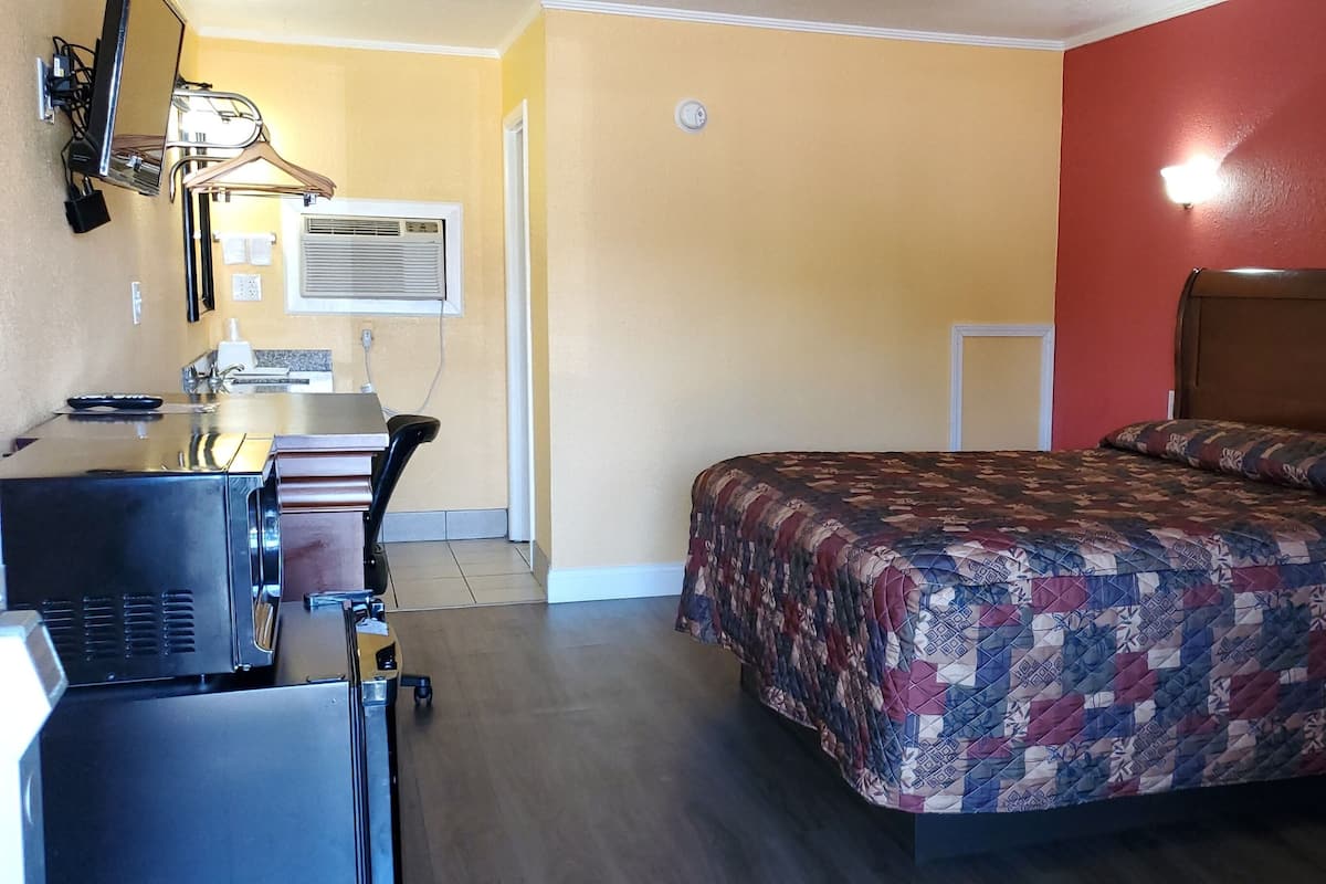 A compact hotel room with a bed, a desk with a computer, a chair, and a small table.