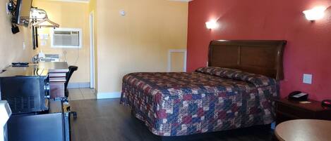 A compact hotel room with a bed, a desk with a computer, a chair, and a small table.