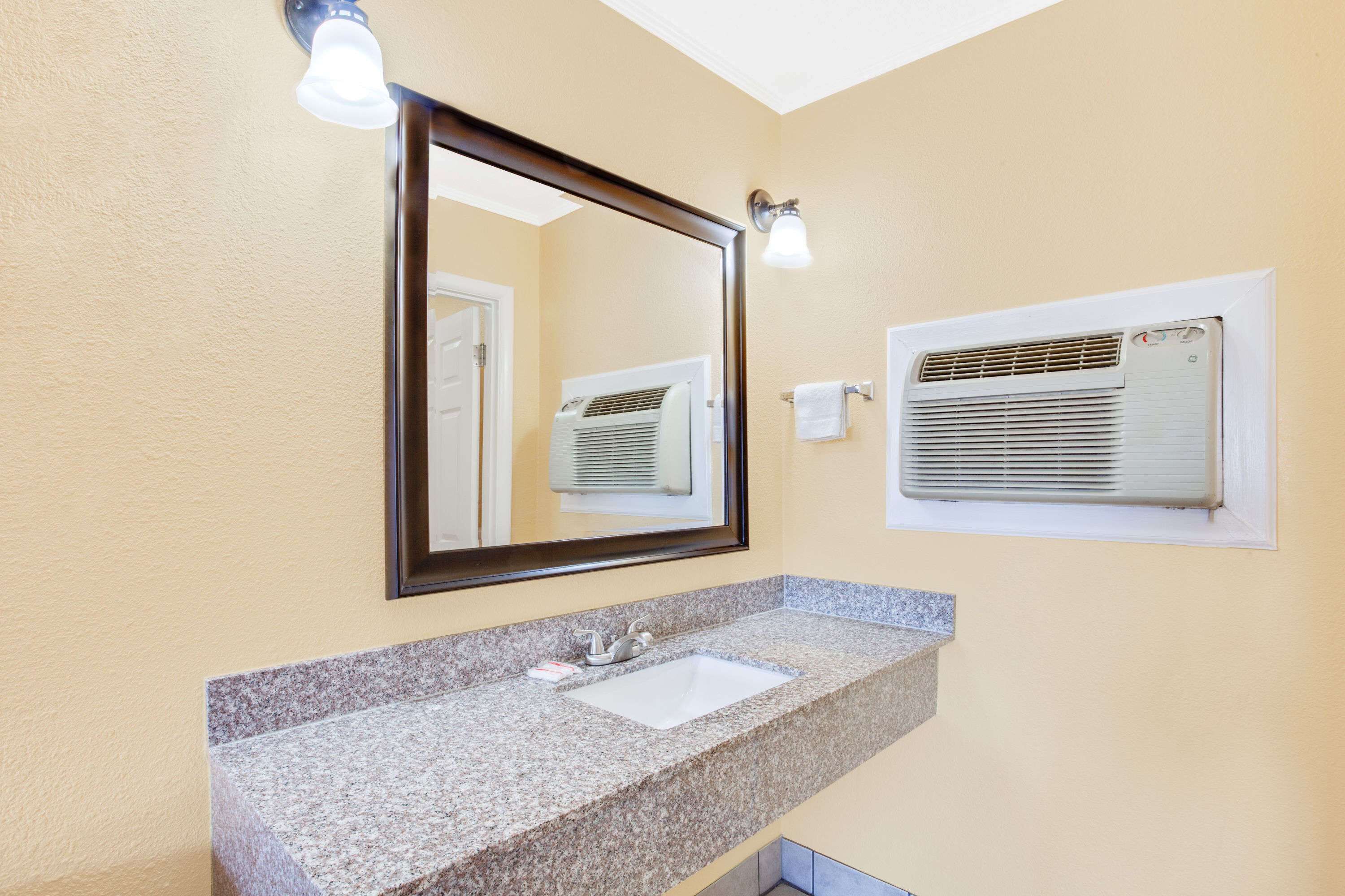 A bathroom with a granite countertop sink, a mirror, and an air conditioning unit mounted on the wall.