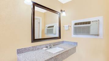 A bathroom with a granite countertop sink, a mirror, and an air conditioning unit mounted on the wall.