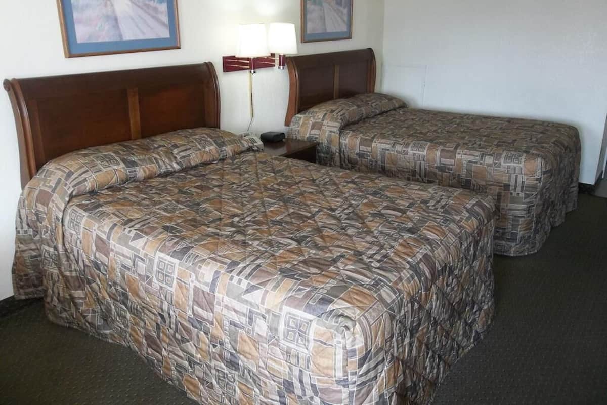 A hotel room with two beds, a nightstand, and two wall-mounted lamps.
