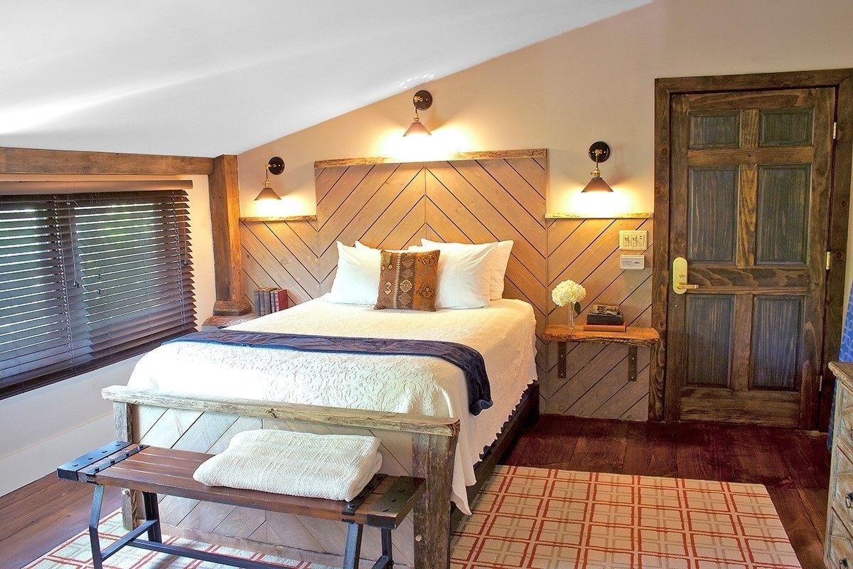 Un dormitorio con cabecera de madera, cama con ropa de cama blanca, un banco con una toalla y una puerta de madera.