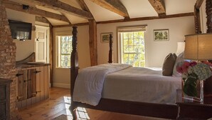 Une chambre avec un grand lit, des poutres en bois, une télévision et une fenêtre donnant sur la forêt.