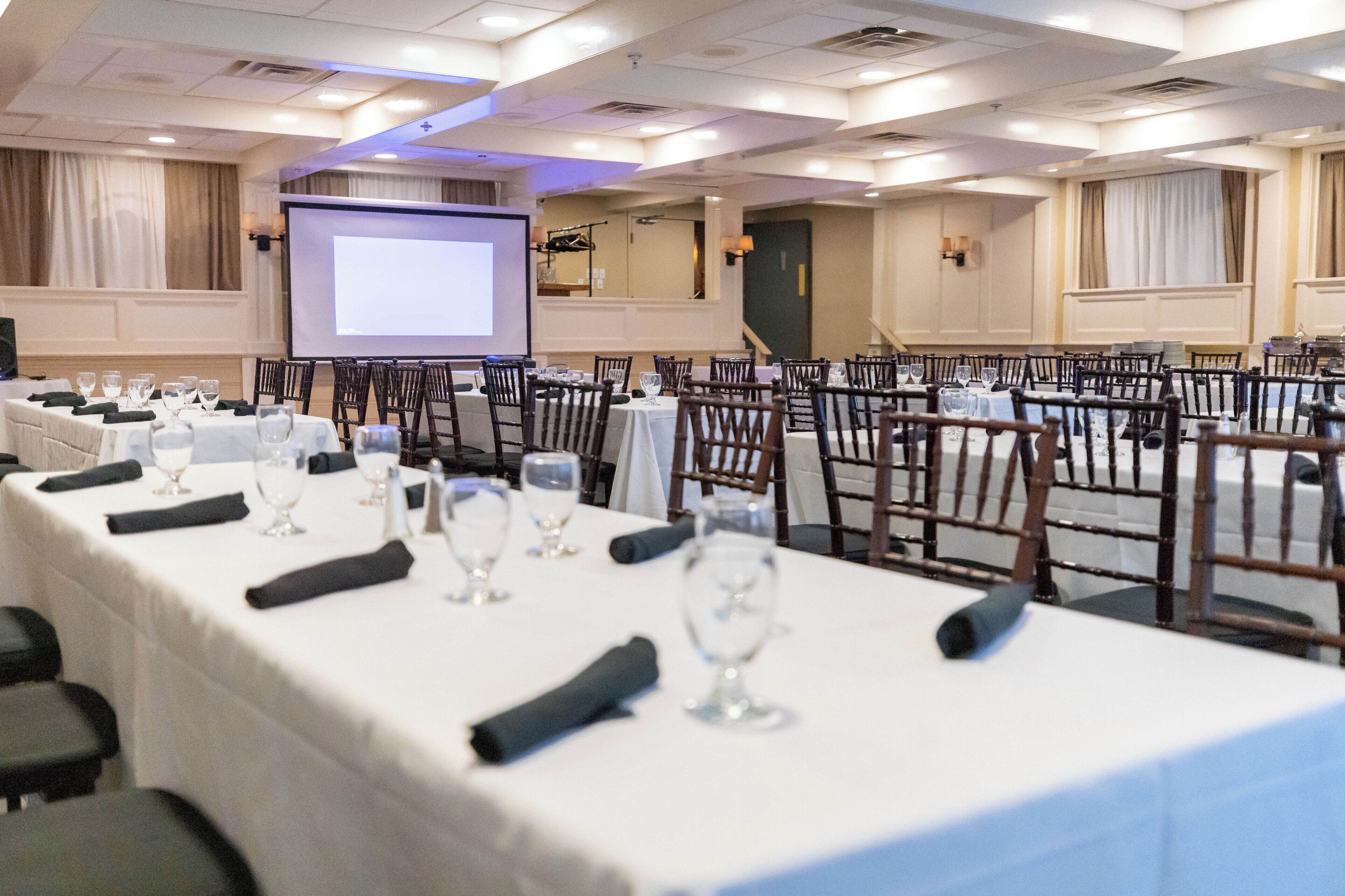 A conference room with tables set for a meeting, a projector screen, and a large screen.