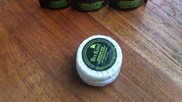 Tres botellas de loción corporal BeeKind y una pastilla de cuidado facial sobre una superficie de madera, con una toalla blanca al fondo.