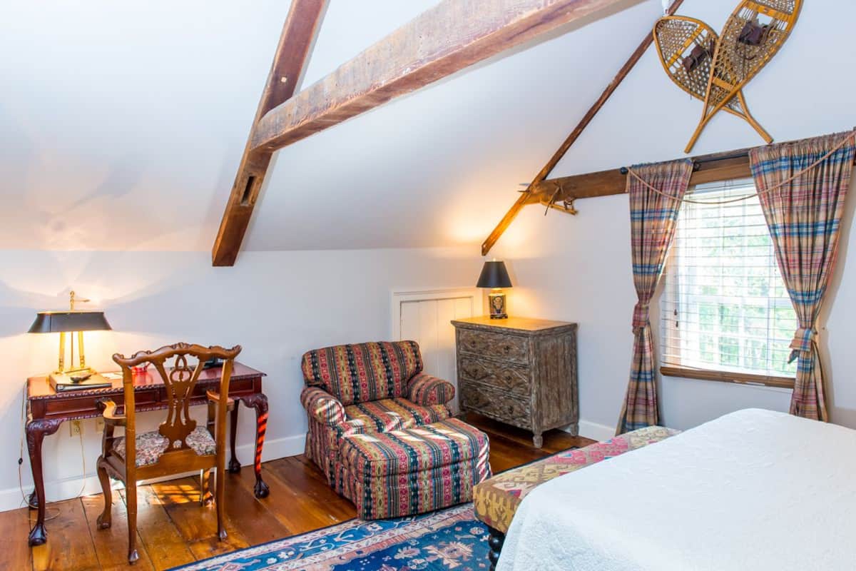 Un dormitorio acogedor con techo de madera, cama, silla, cómoda y ventana con cortinas.