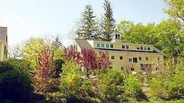 Un bâtiment à deux étages, entouré d’une végétation luxuriante et d’arbres.