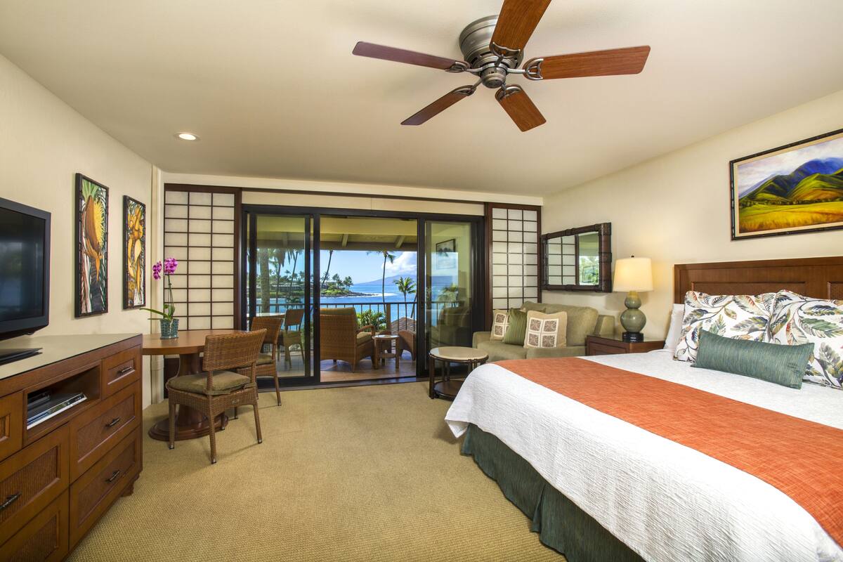 Quarto de hotel com cama, televisão, secretária e varanda vista para o mar.