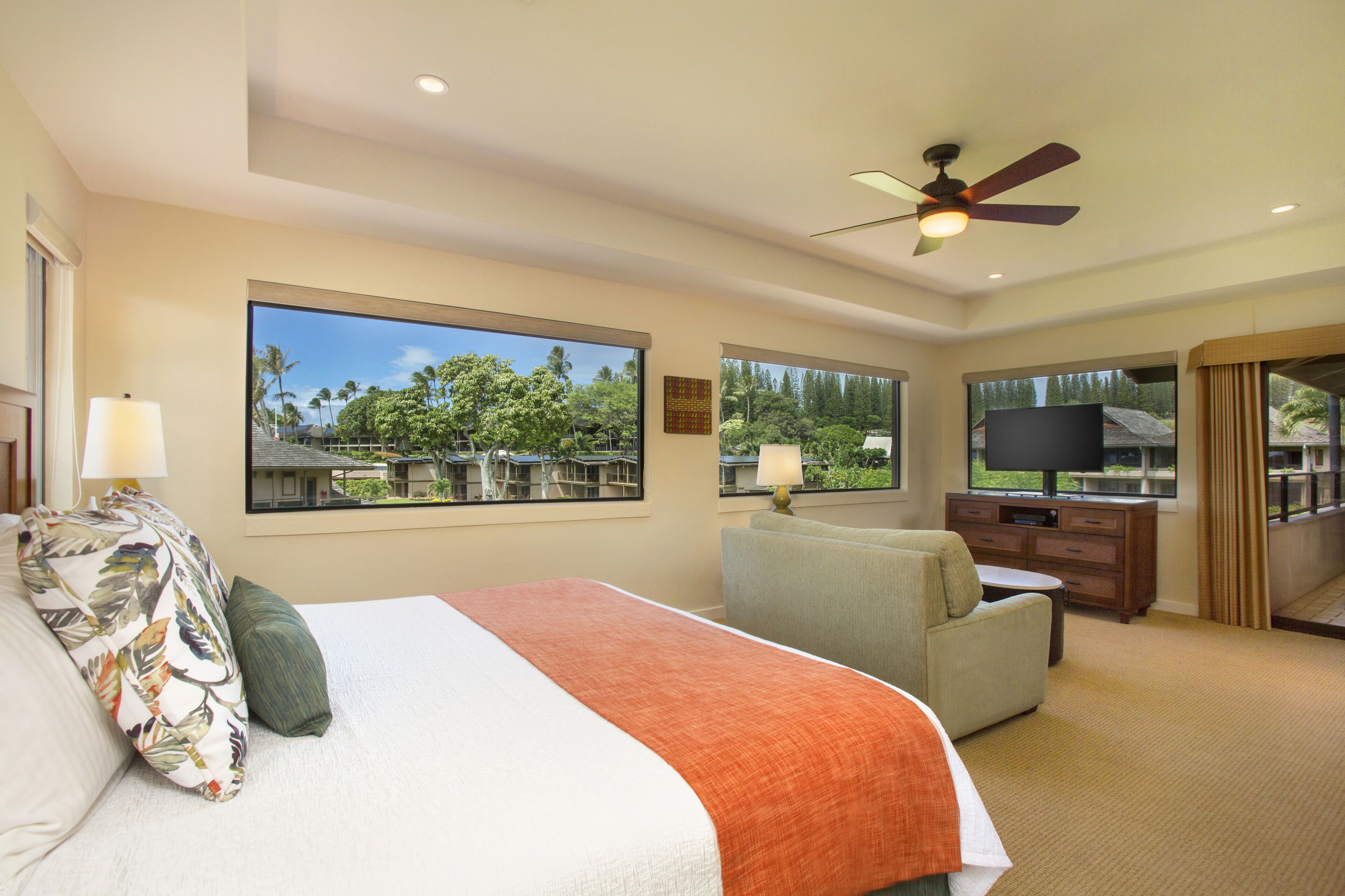 A hotel room with a large bed, a sofa, a TV, and a ceiling fan.