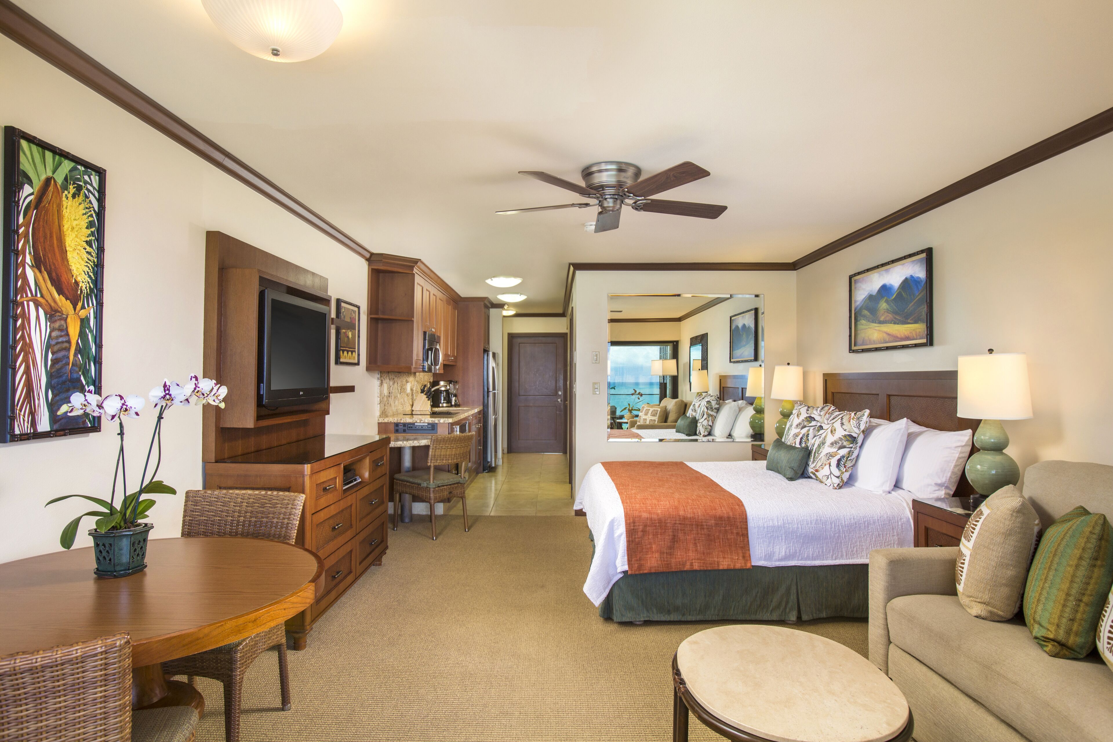 A hotel room with a bed, a sitting area with a sofa and a table, a kitchenette, and a television.