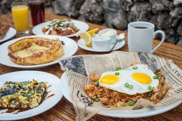 Una mesa de desayuno con diferentes platos, incluyendo arroz frito, una quiche y una ensalada de frutas.