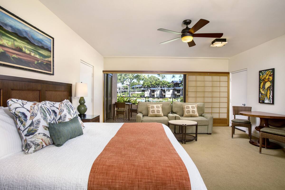 Quarto de hotel com uma cama, um sofá, uma mesa de jantar e vista para o exterior.