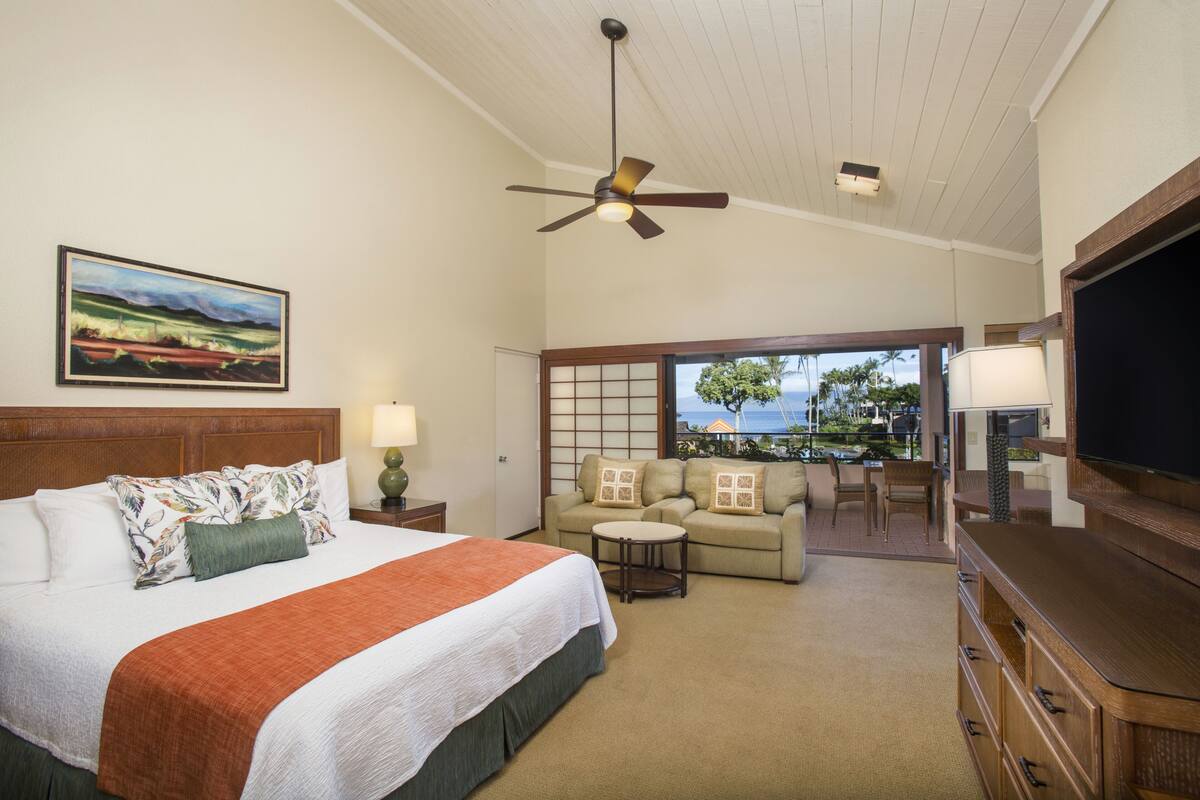 Quarto de hotel com cama, sofá, televisão e ventilador de teto.