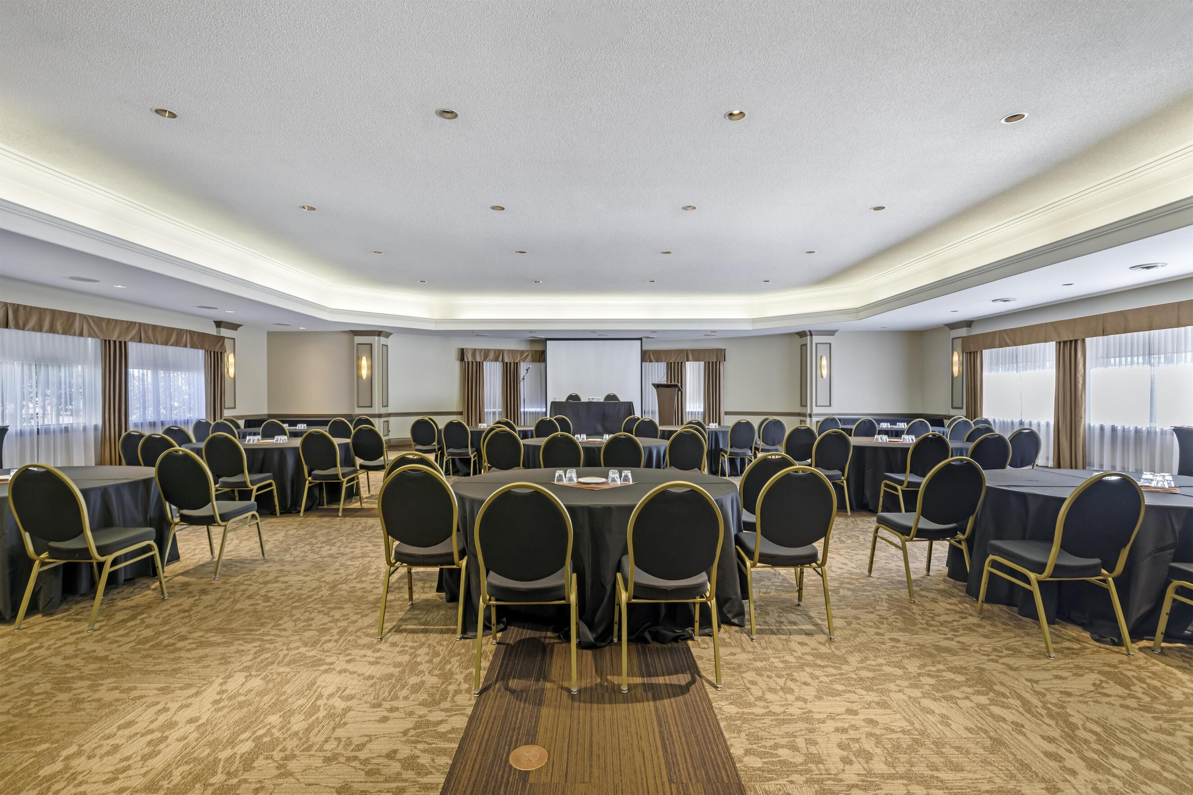 A large conference room with round tables and chairs, carpeted floor, and a white ceiling with recessed lighting.
