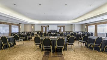A large conference room with round tables and chairs, carpeted floor, and a white ceiling with recessed lighting.