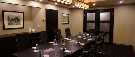 A conference room with a long table, chairs, framed artwork on the walls, and ceiling lights.