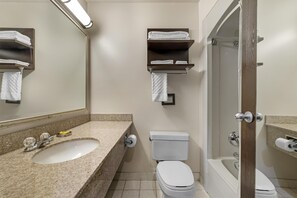 Un baño con lavabo, inodoro y bañera. Hay repisas con toallas sobre el inodoro y un espejo sobre el lavabo.