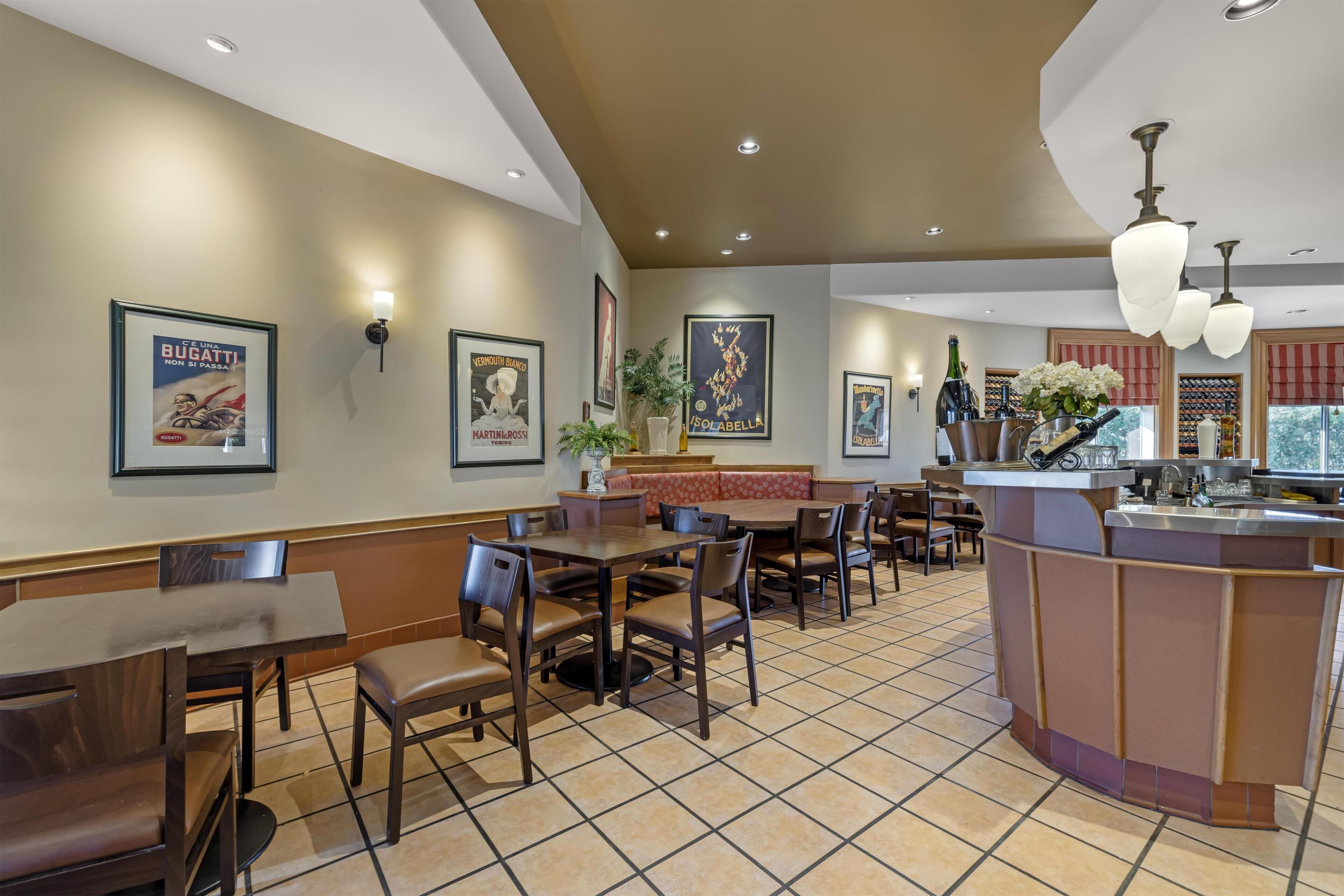 A restaurant with multiple tables and chairs, a bar area, and framed pictures on the walls.