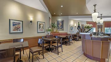 A restaurant with multiple tables and chairs, a bar area, and framed pictures on the walls.