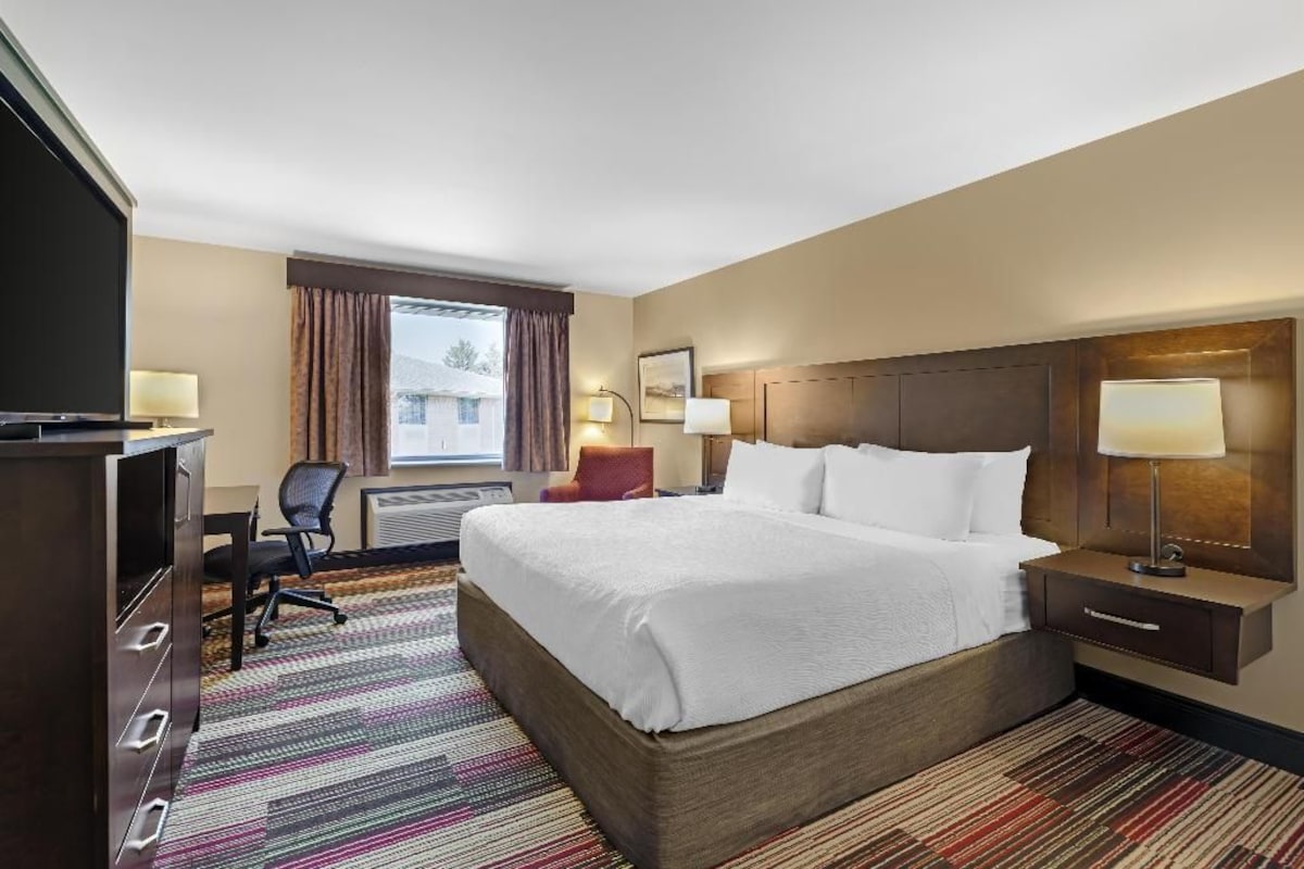 A hotel room with a large bed, a desk with a chair, a television, and a window with curtains.