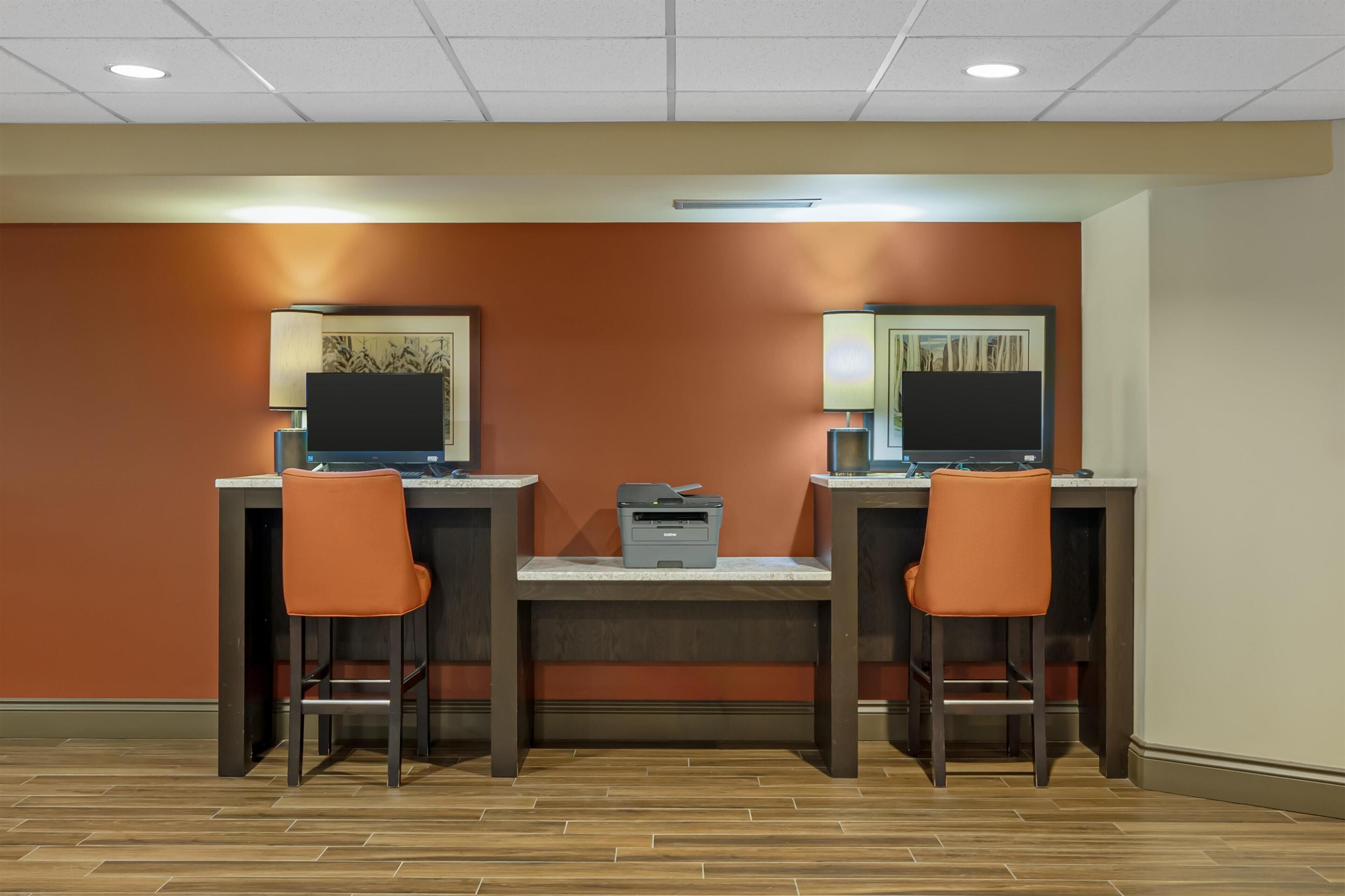 A room with two desks, each with a computer and a chair. There is a printer on the central table.