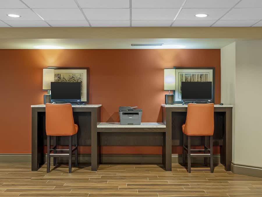 Una habitación con dos escritorios, cada uno con una computadora y una silla. Hay una impresora en la mesa central.